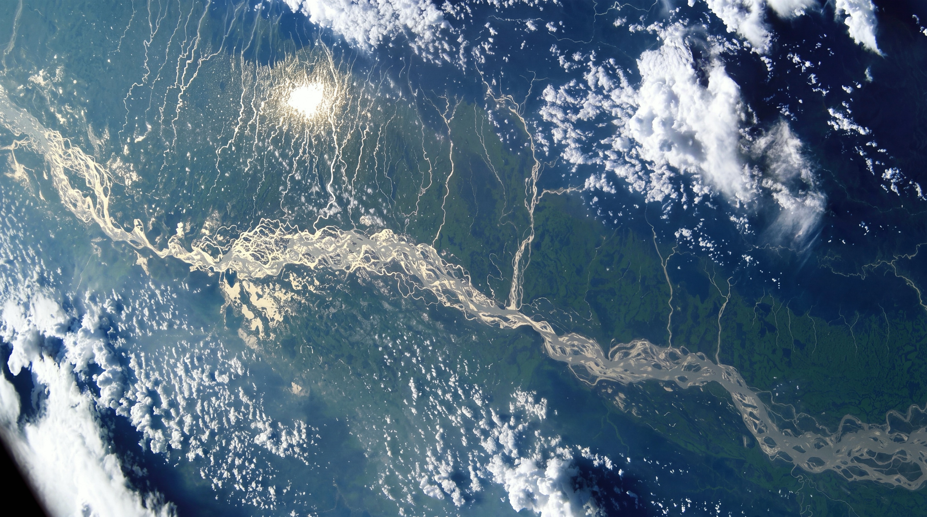 Northeast India from space: a braided river winding through green floodplain under scattered clouds. NASA photograph ISS005-E-16618, taken from the International Space Station in 2002