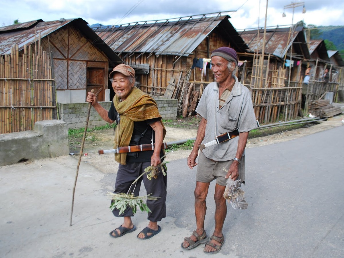 Two Apatani elders in cane hats walking down a village street