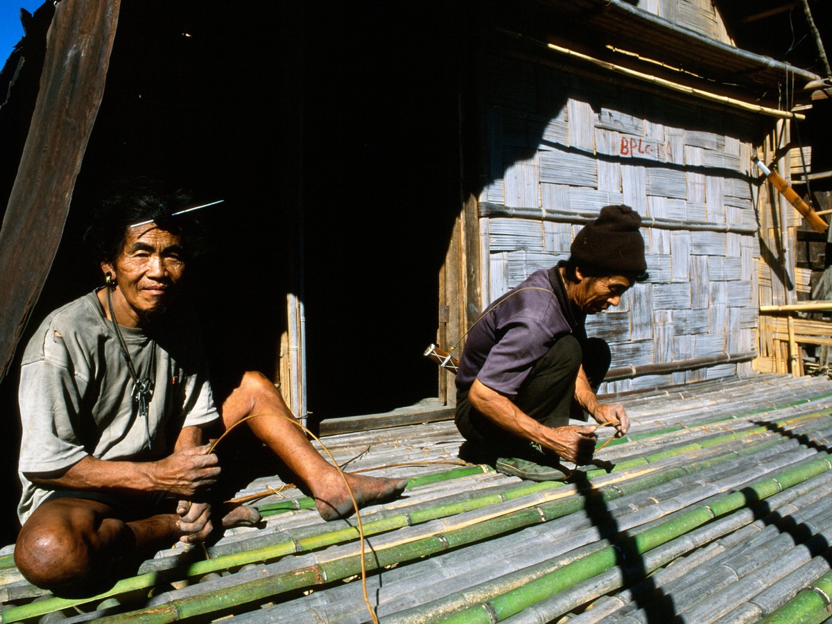 Two men splitting bamboo on the porch of a village house