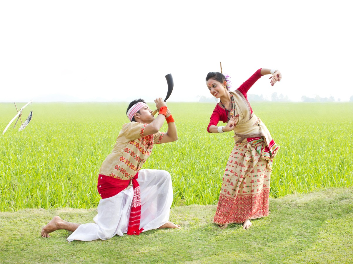 Bihu dancers in traditional dress performing in a green paddy field