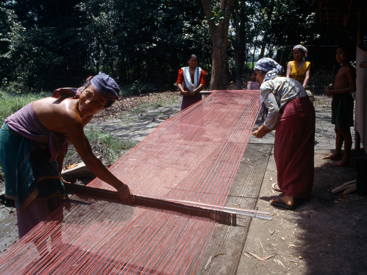 Women stretching and weaving a long length of cloth in a village