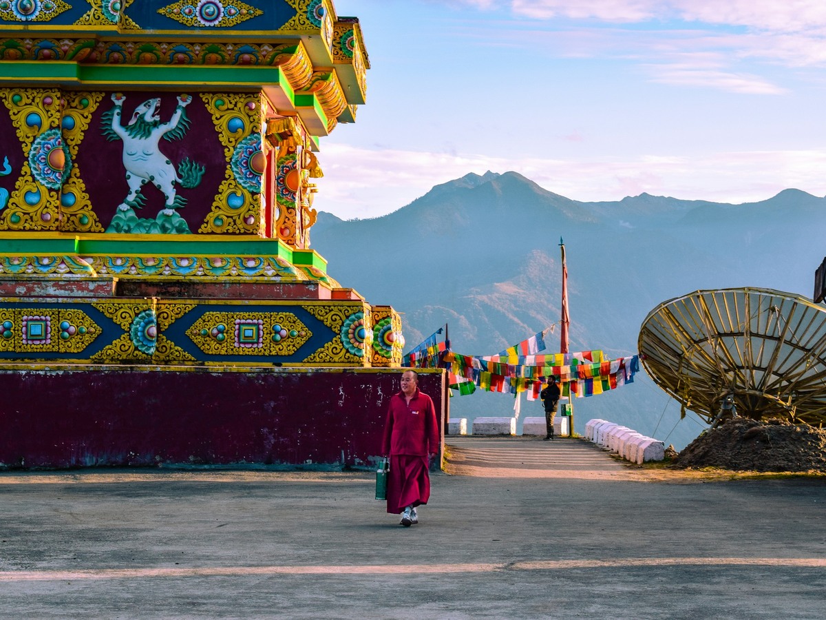 A monk walking past a painted stupa, mountains behind