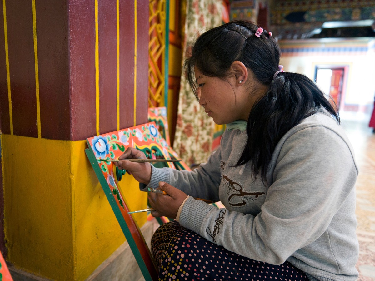 A woman painting a monastery doorway by hand in bright colors