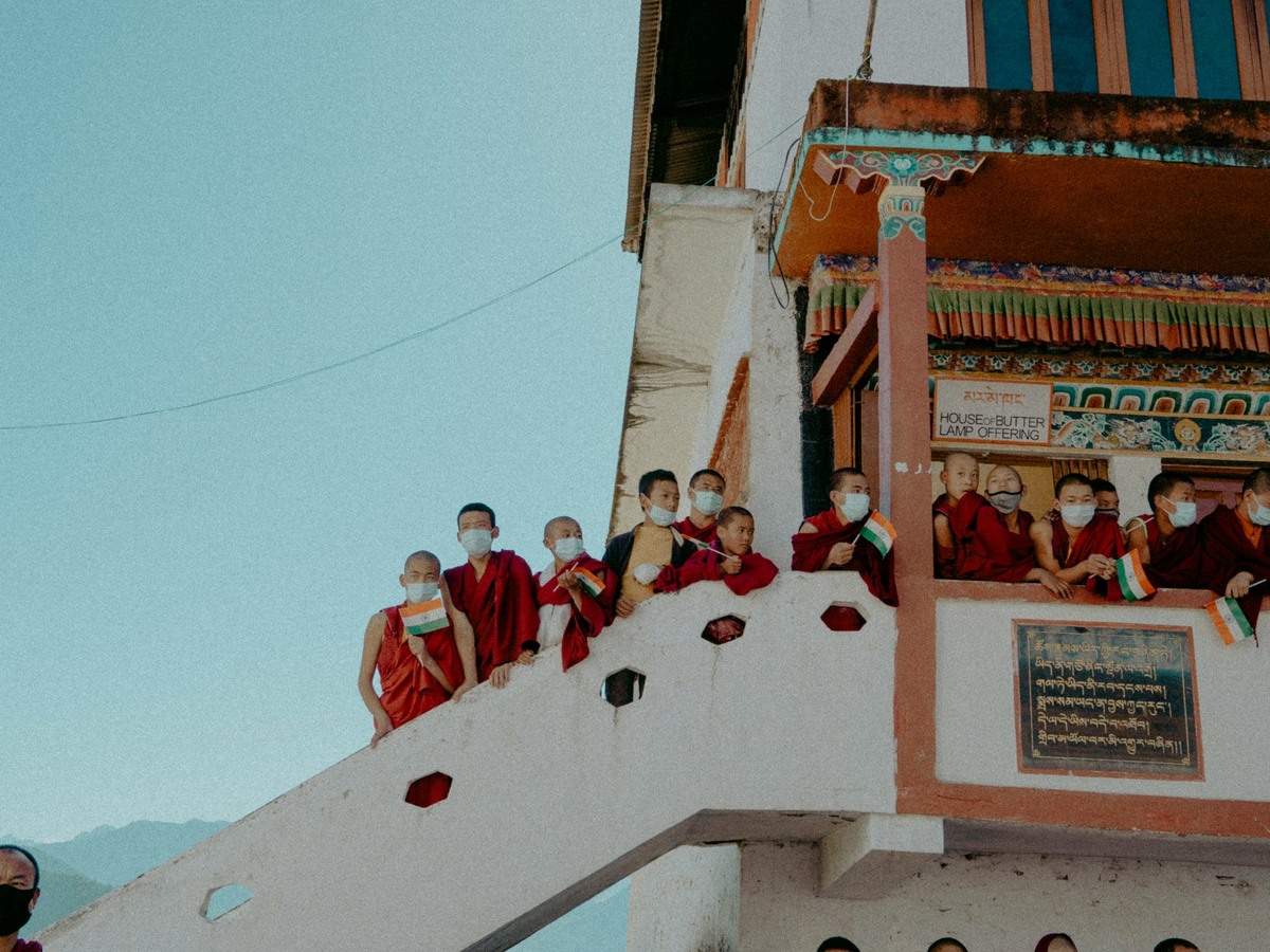 Young monks in maroon robes looking down from a monastery balcony