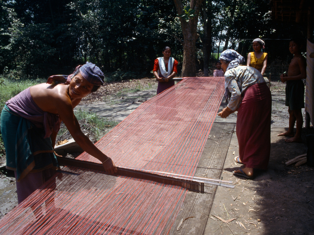 Women stretching warp threads for weaving outside a village house