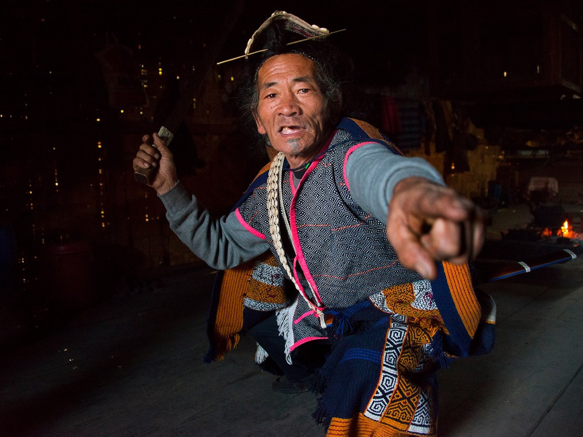 An elder in a cane hat telling a story beside the hearth