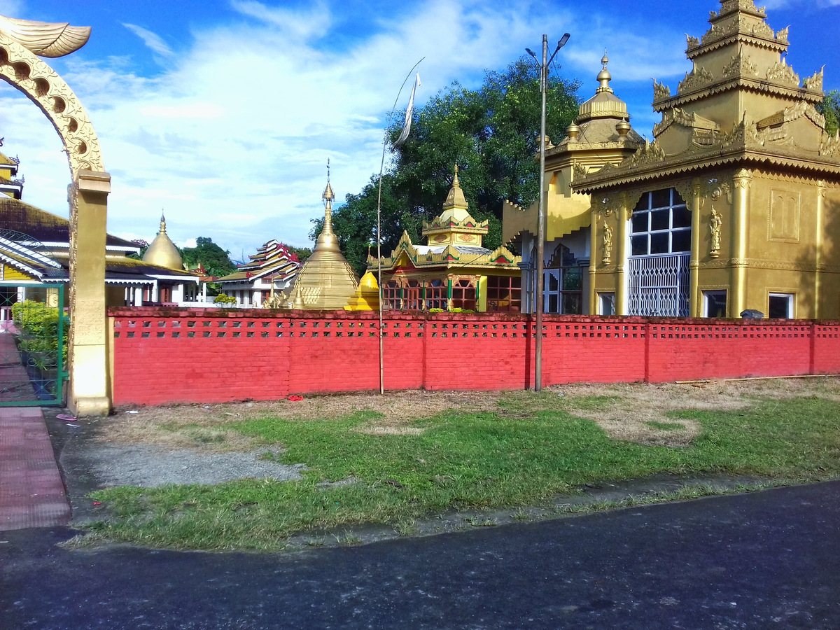 A golden Buddhist monastery behind a red gateway in Tezu