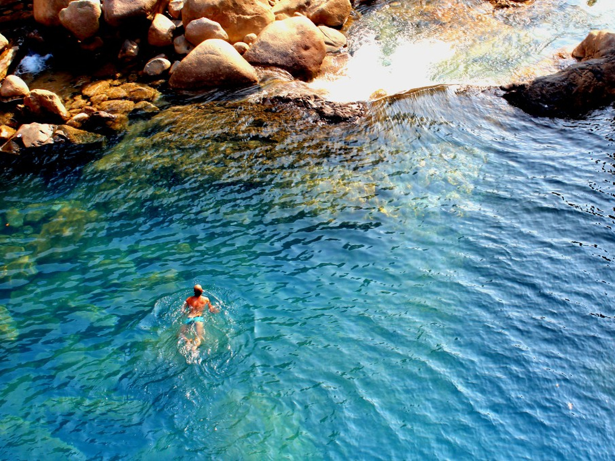 A swimmer in a clear blue natural pool among boulders