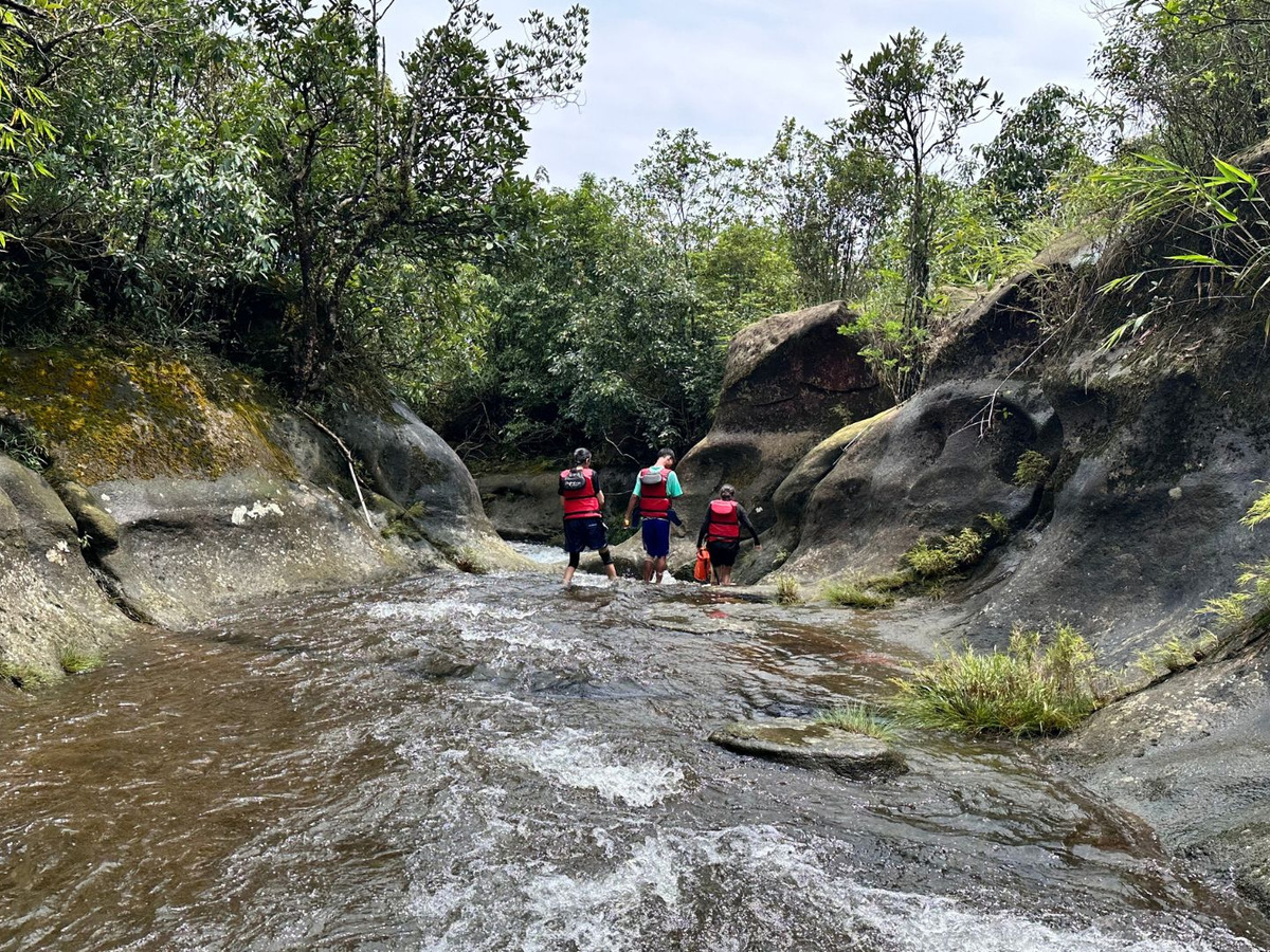 Trekkers in life jackets wading up a rocky river channel