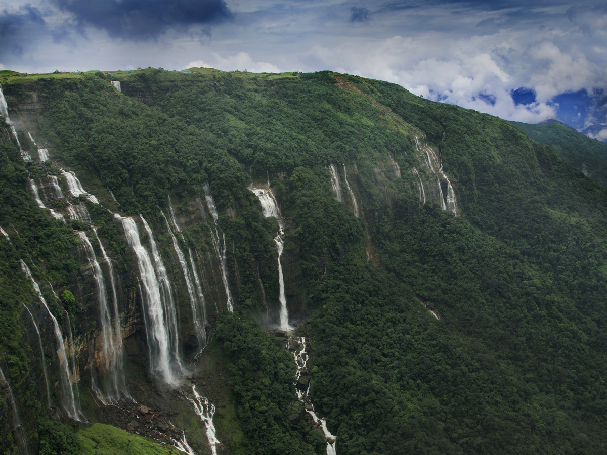 Several waterfalls pouring off a long green cliff