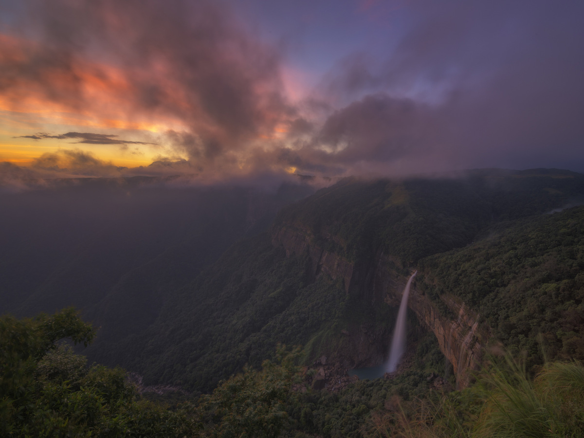A waterfall dropping into a gorge under a red sunset sky