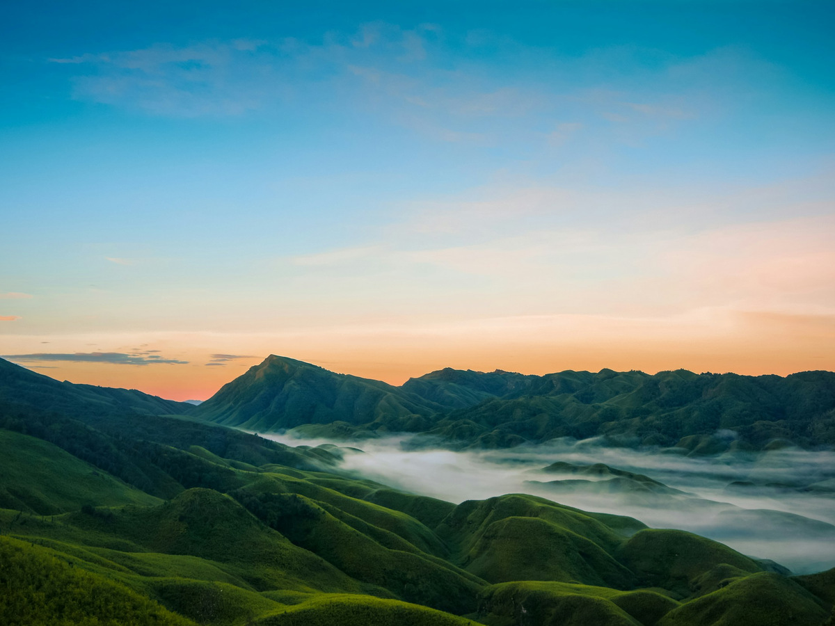 Mist filling a valley of green hills at dawn