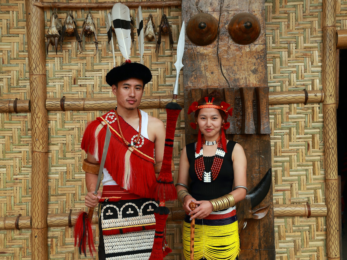 A young man and woman in traditional Naga dress in front of a carved wall