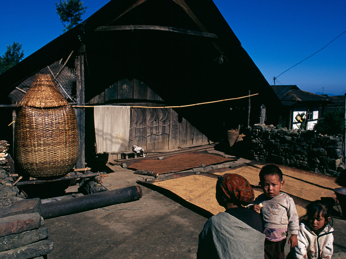 Children beside a large cane grain basket outside a thatched village house