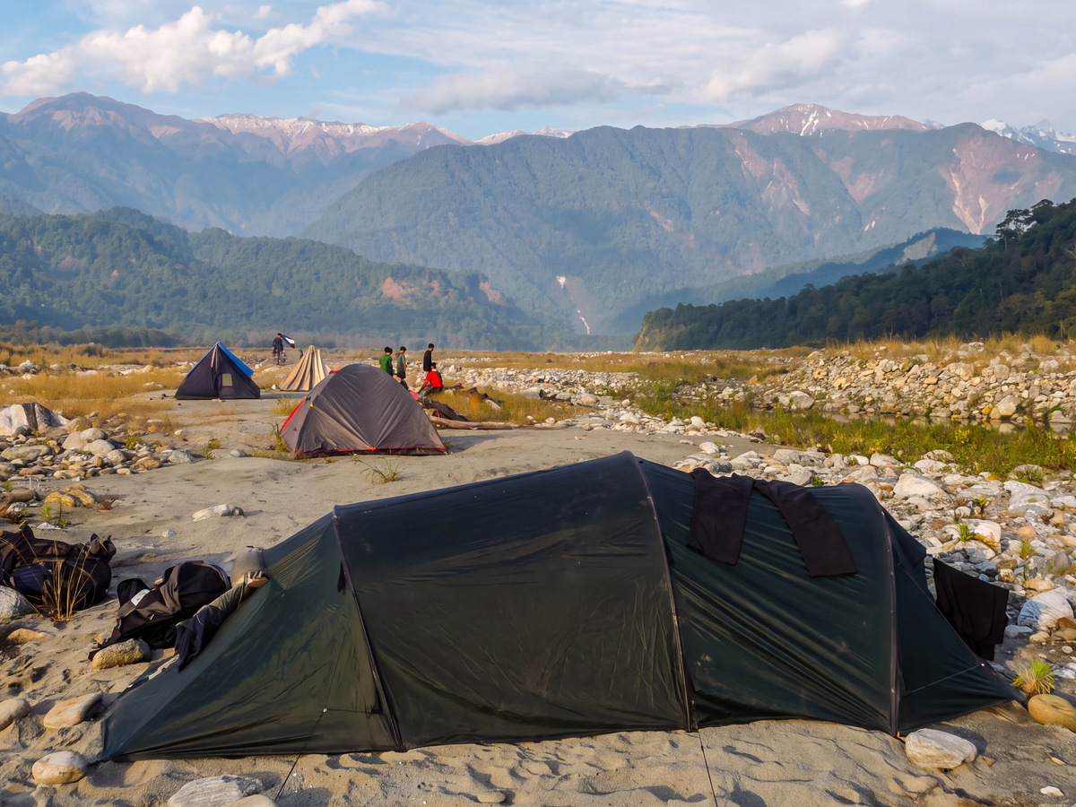 Tents pitched on a stony riverbed with snow peaks behind