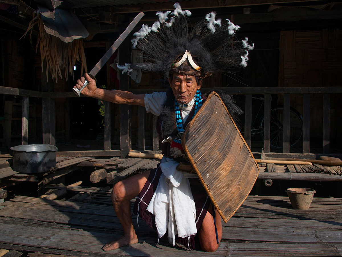 An Adi elder in a hornbill-feather headdress holding a sword and shield
