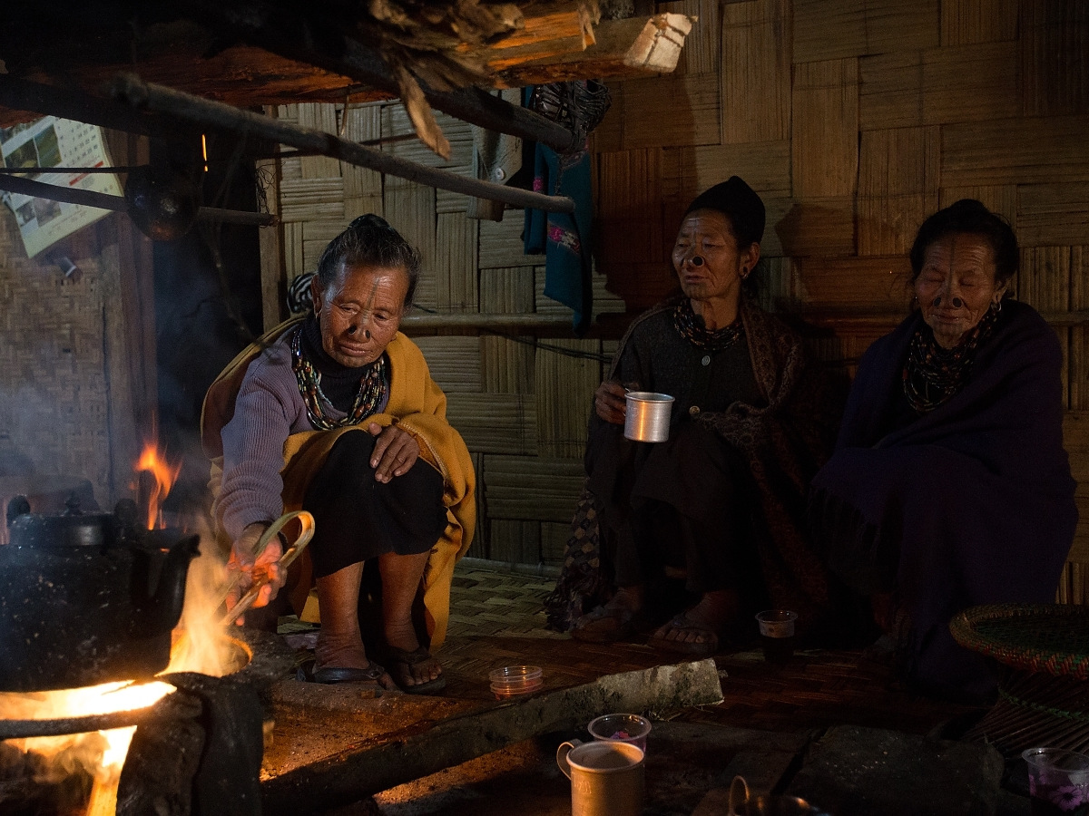Three women sitting around a cooking fire inside a bamboo house