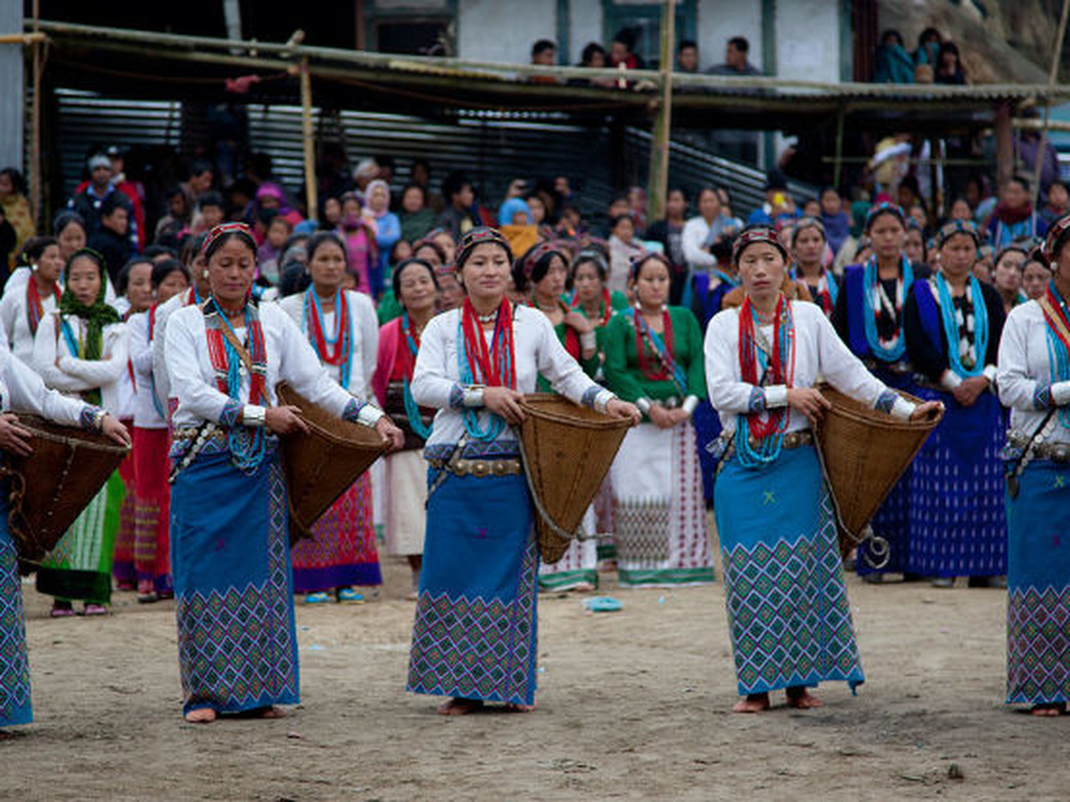 Women in blue woven skirts and white blouses dancing with cane baskets at a village festival