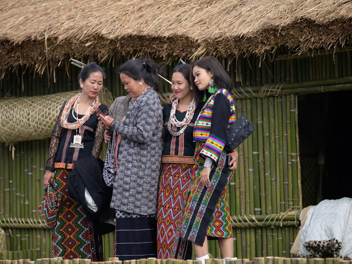 Idu Mishmi women in traditional woven dress outside a bamboo house