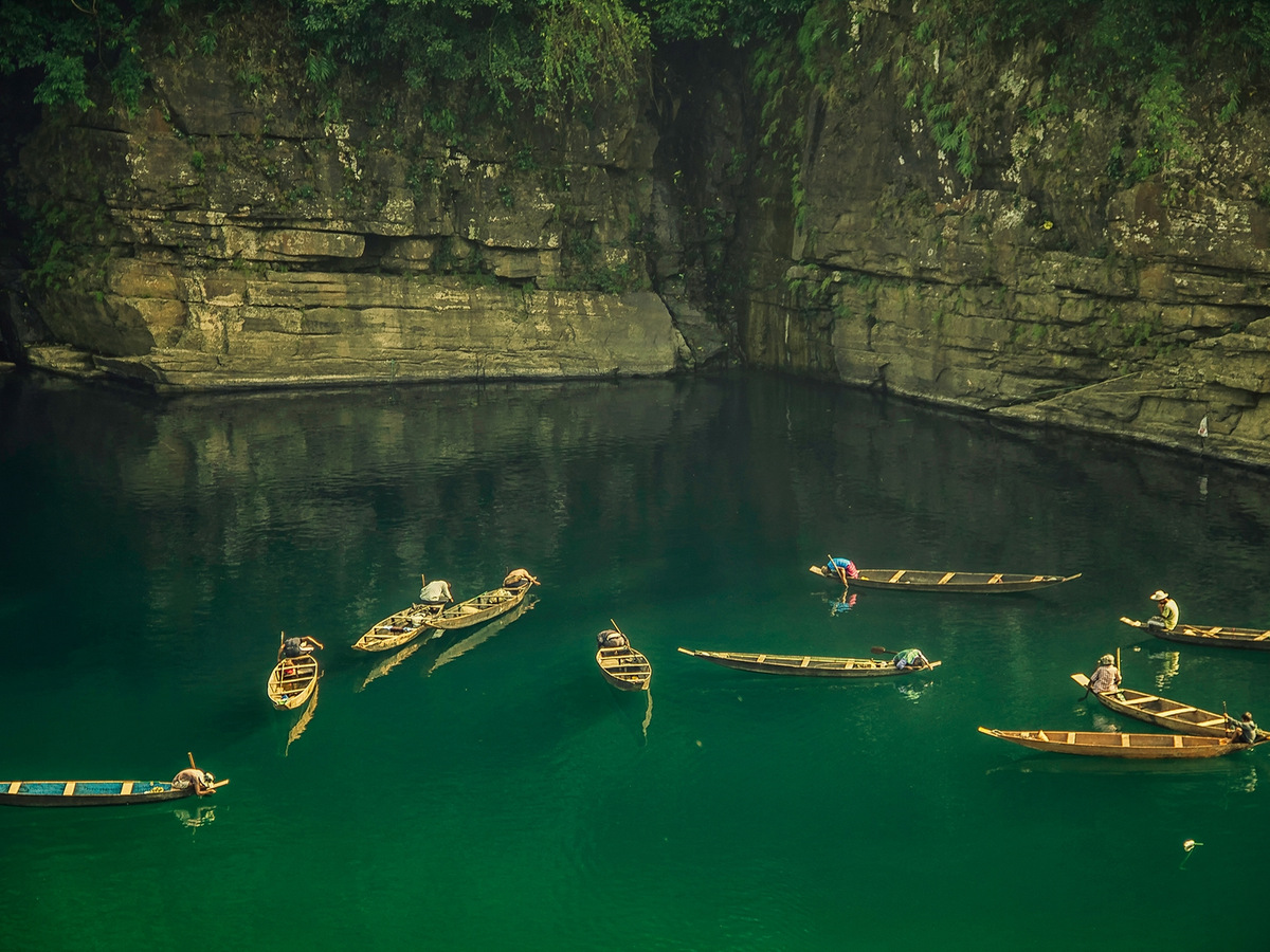 Country boats on the clear green Umngot river below steep cliffs