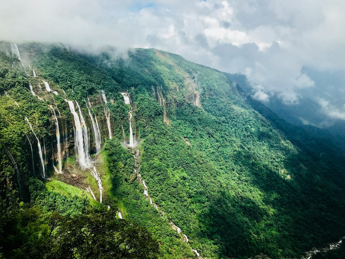 Many waterfalls dropping off a long green cliff