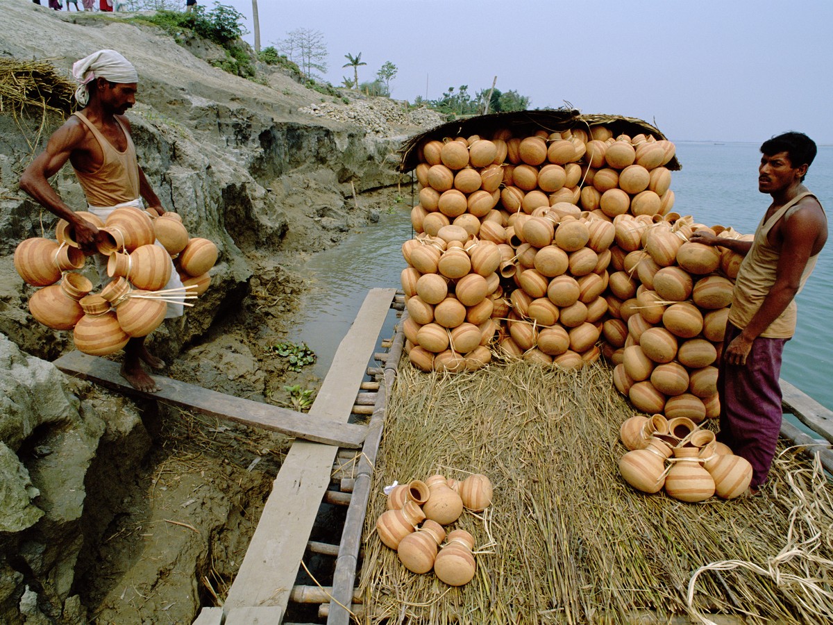 Potters loading stacks of earthenware onto a boat at the riverbank