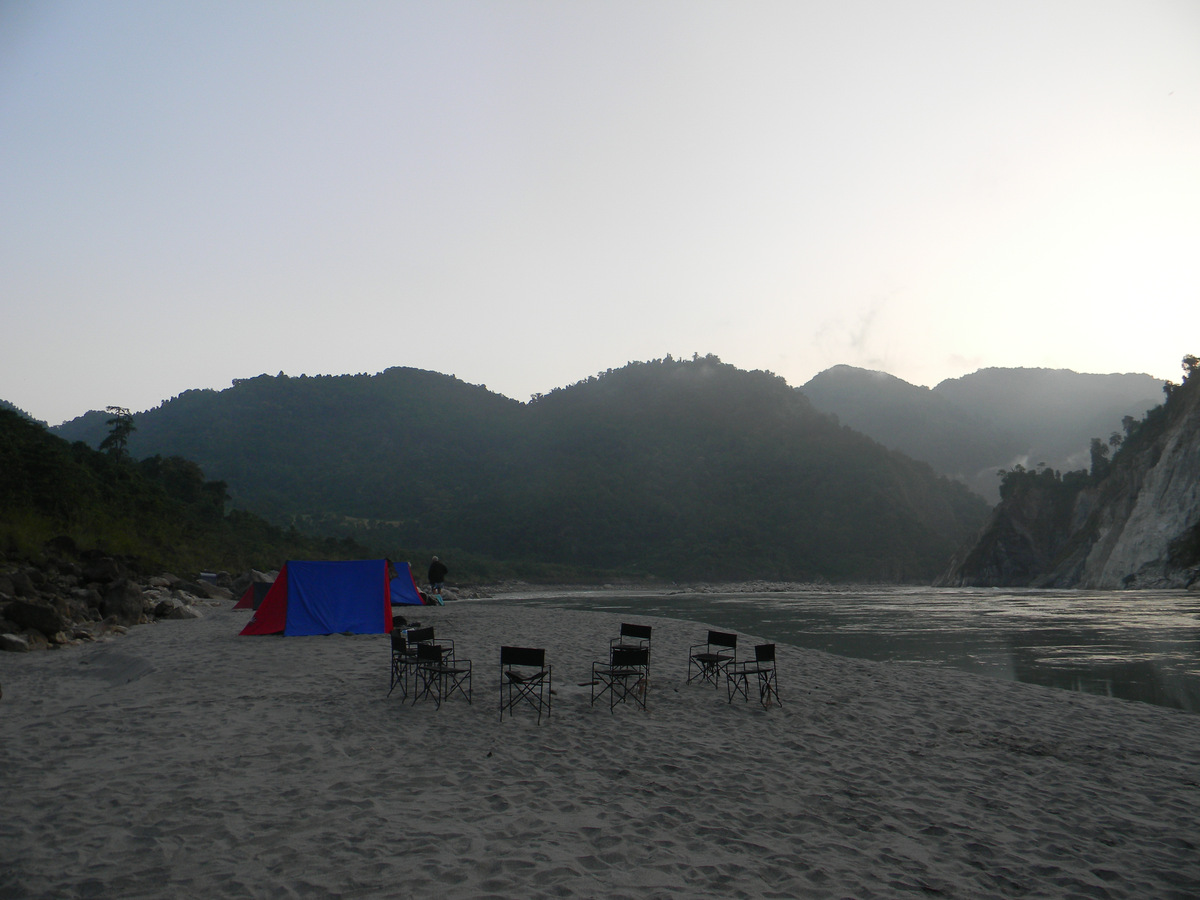 Tents and camp chairs on a sandy river beach at dusk