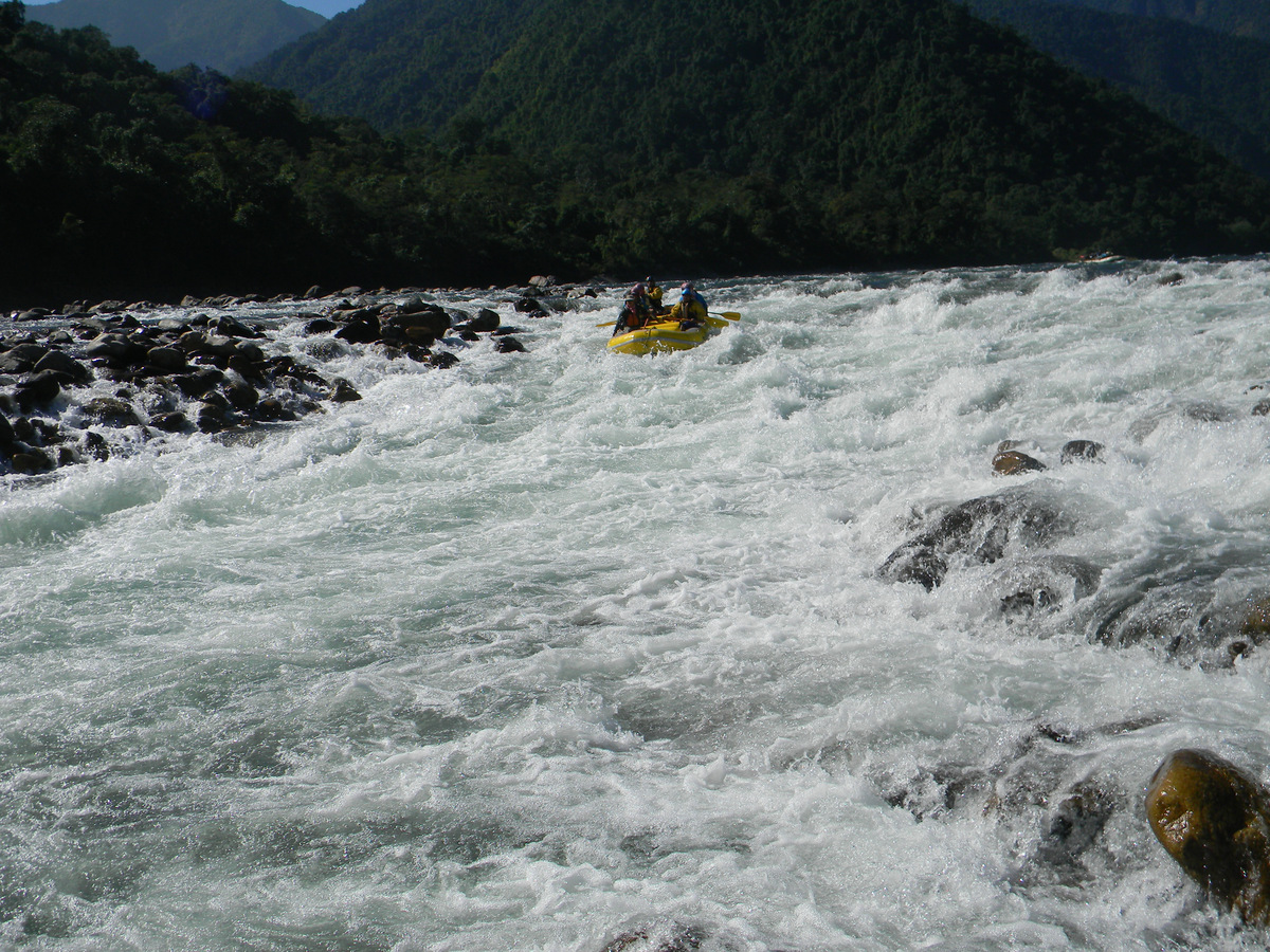 A yellow raft running white water below forested mountains