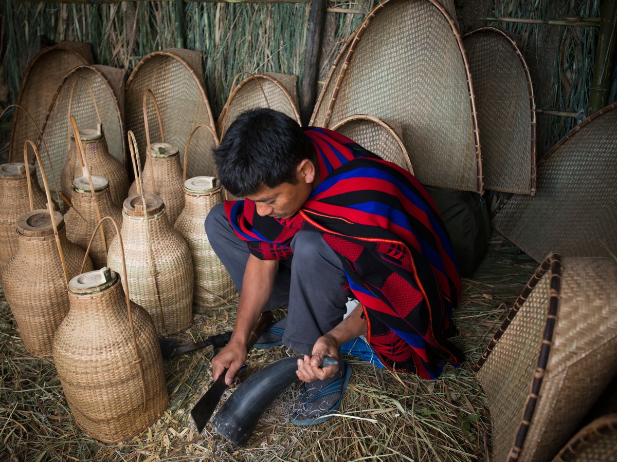 A man weaving bamboo fish traps and carrying baskets outside his house