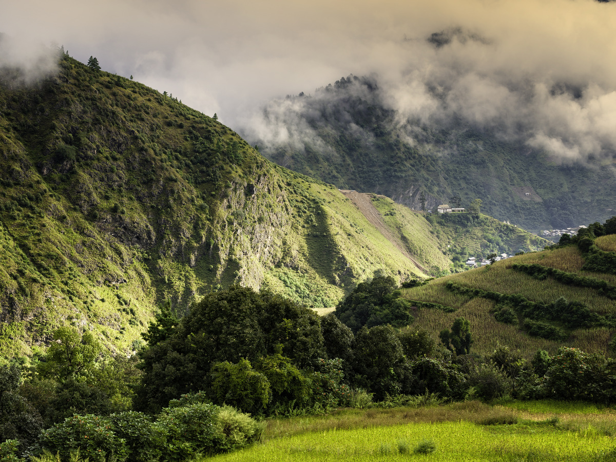 A green valley under a sunlit cloud-topped ridge