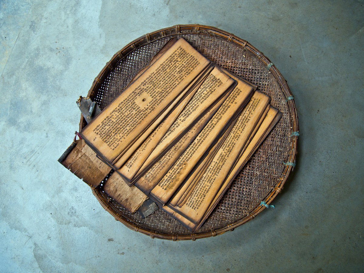 Hand-inked sanchipat manuscripts on a woven tray at a Majuli satra