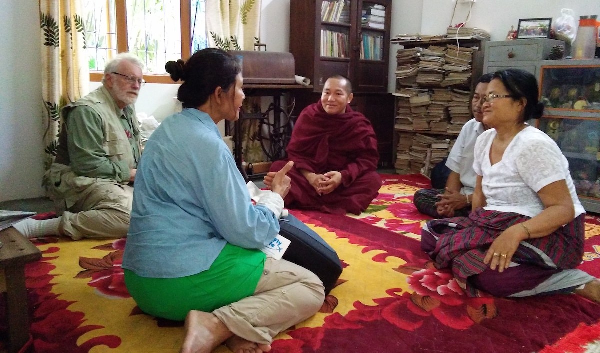 Travelers sitting with a monk and villagers on a rug