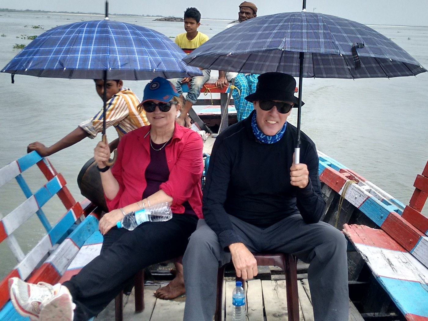 Travelers under umbrellas on a boat on the Brahmaputra, with the boatmen behind